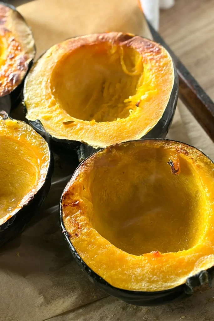 The roasted acorn squash with flesh side up on a parchment paper lined baking sheet.