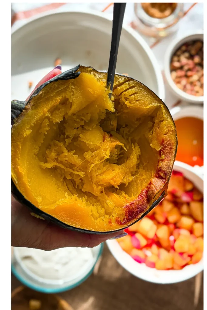 Someone hold up a cooked acorn squash halve with a fork in it, the flesh being shredded.
