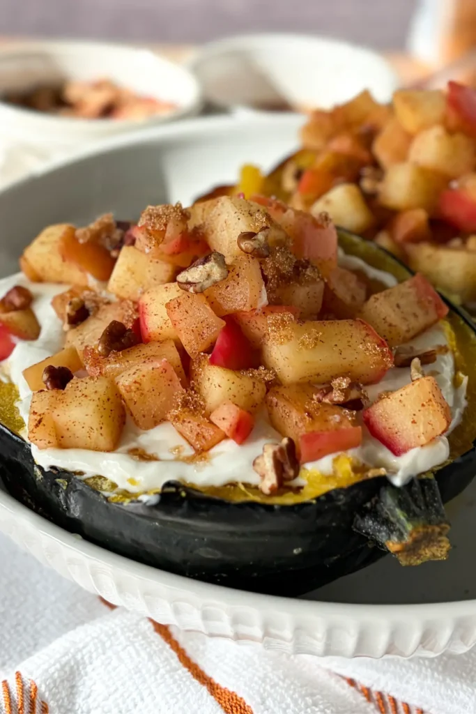 Two fully assembled acorn squash breakfast boats on a white plate on a brown and white striped towel on a table.