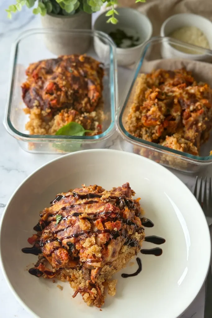 A large slice of cheesy Italian casserole drizzled with balsamic glaze on a white plate next to two meal prep storage containres with a slice of casserole in each one.