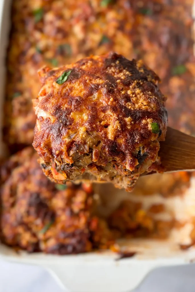 A close-up of a big slice of lentil quinoa casserole on a wooden spoon right over the large casserole dish.