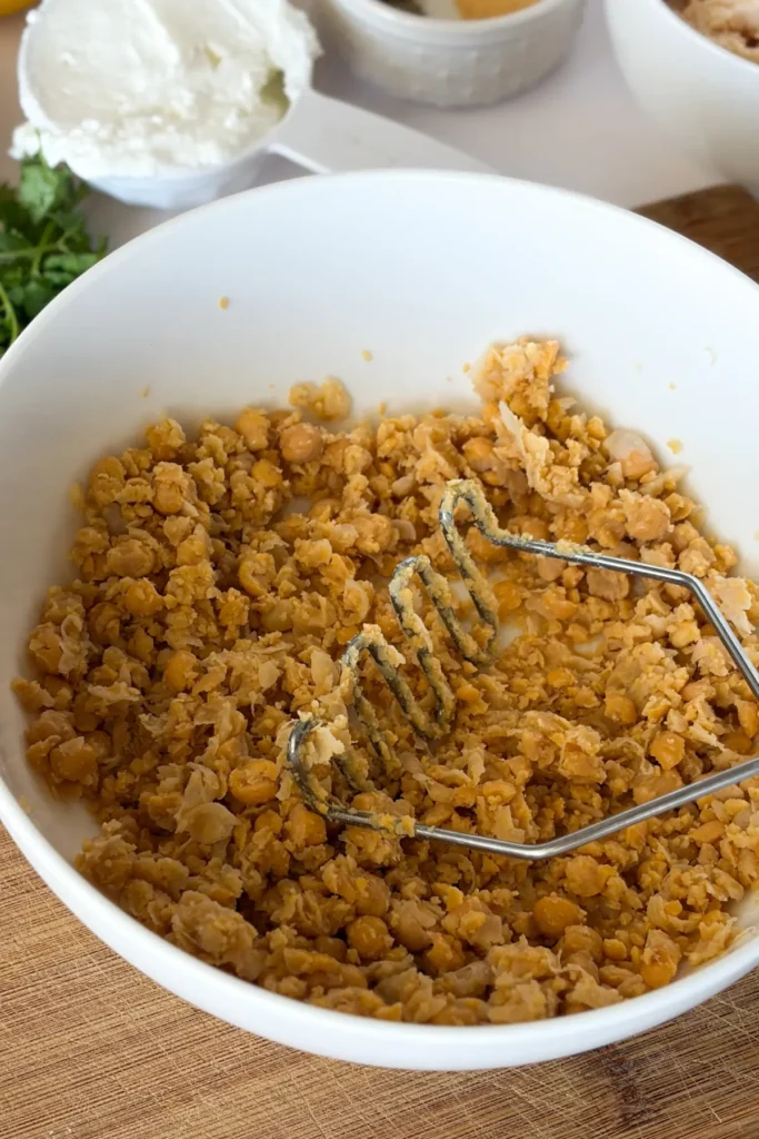 A bowl of mashed chickpeas with the potato masher in it.