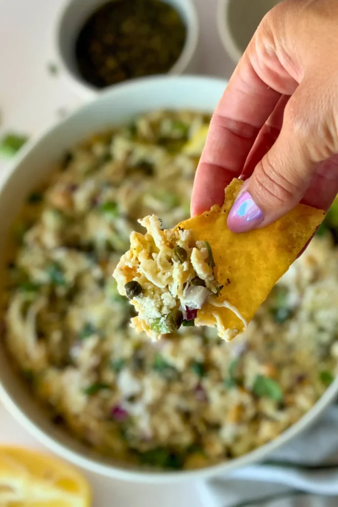 Chicken salad on a tortilla chip in someone's hand with the big bowl in the background.