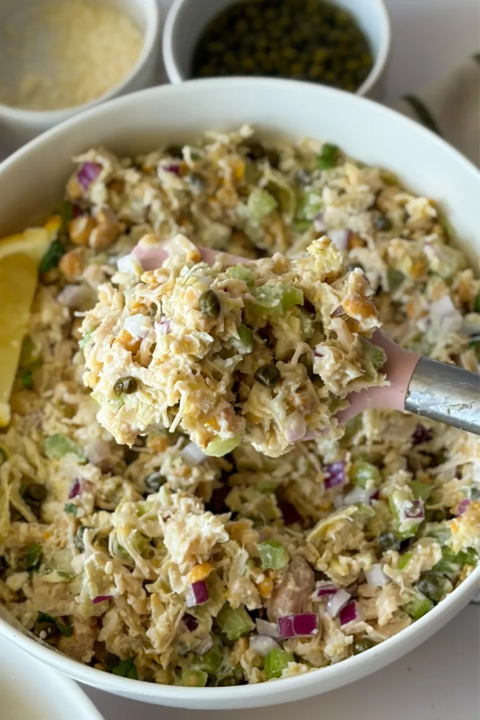 A close-up of a spatula full of chicken salad over a large bowl.