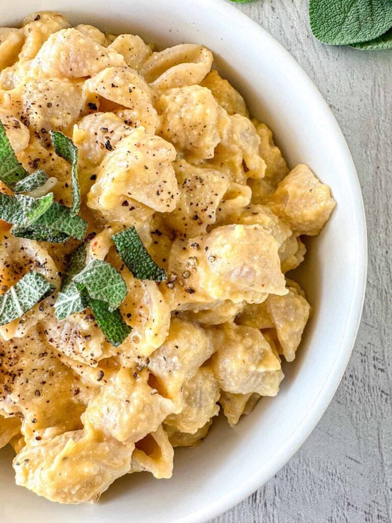 A close-up of a bowl o butternut squash and feta pasta on a table.