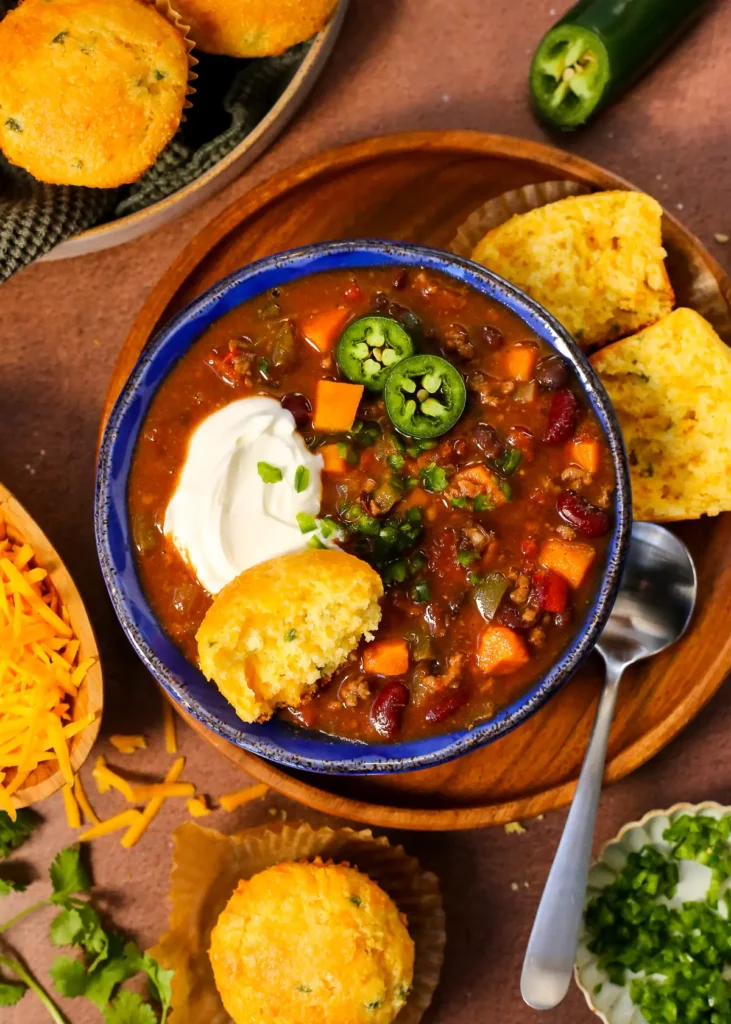 A bowl of butternut squash chili topped with cornbread and yogurt on a table.