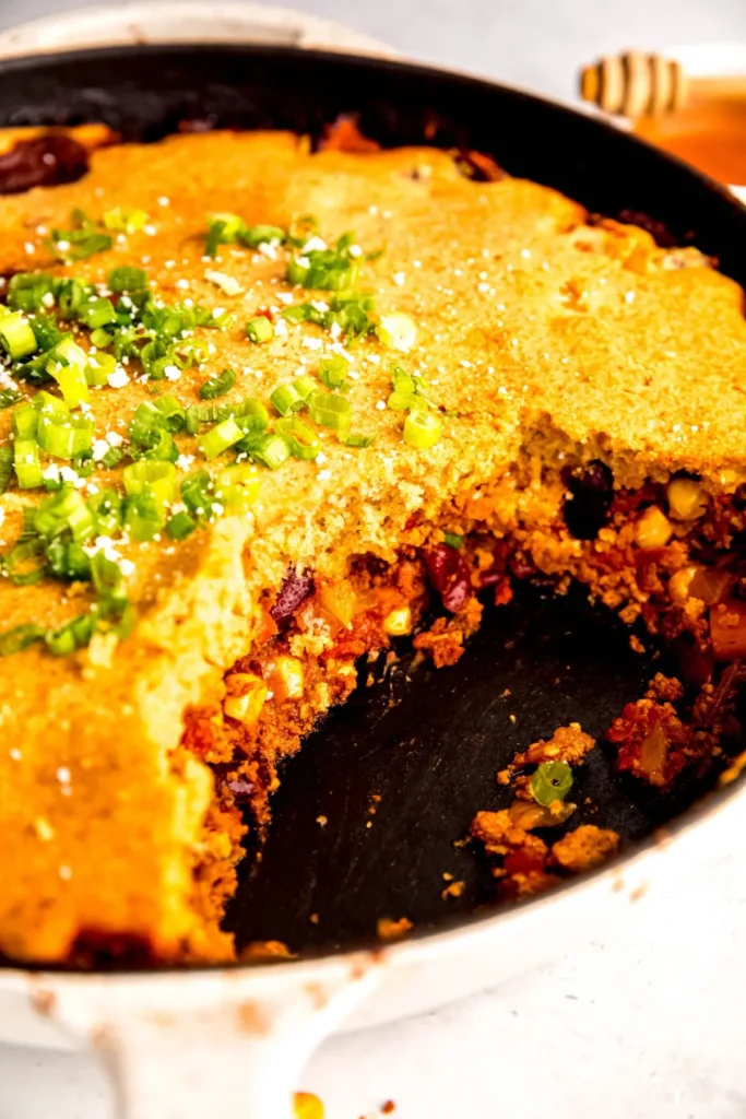 A close-up of the cornbread chili casserole with a large piece removed in a skillet on a table.