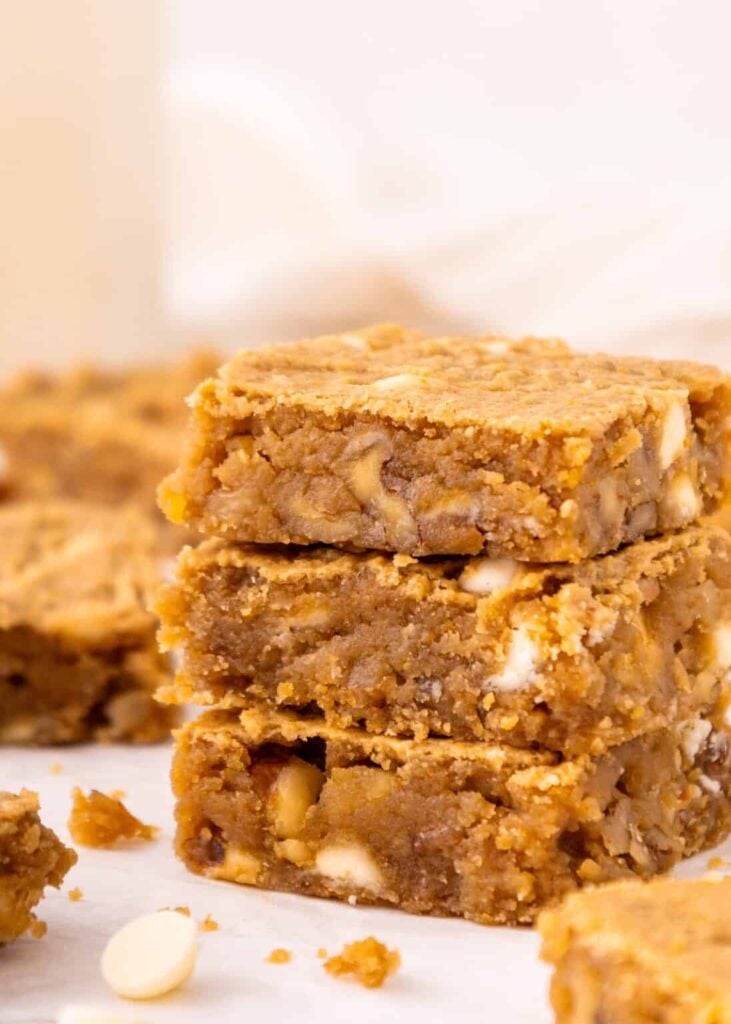 Three chickpea blondies stacked on top of one another on a cutting board.