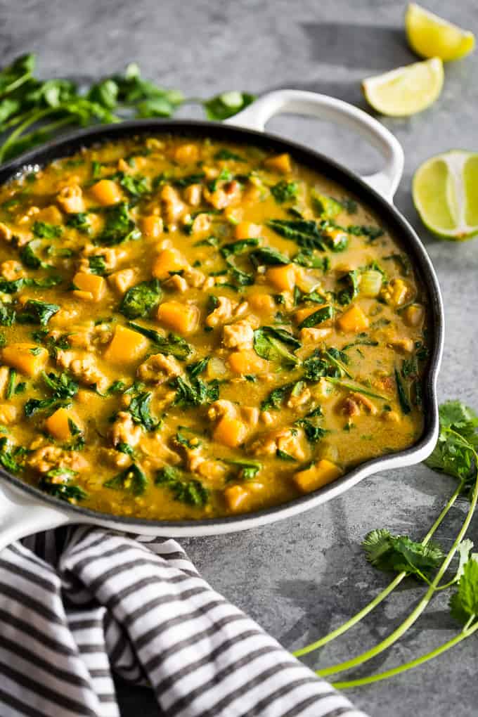 Coconut curry and vegetables in an iron skillet on a counter next to lime wedges.