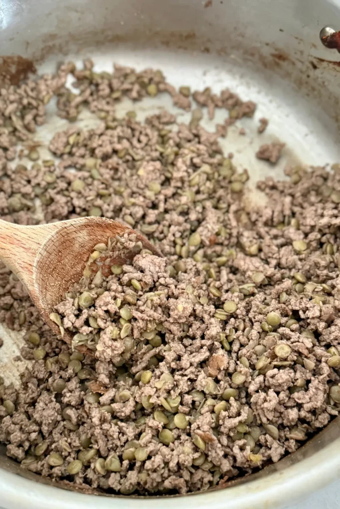 Ground beef cooked into a pot with lentils and a wooden spoon. 