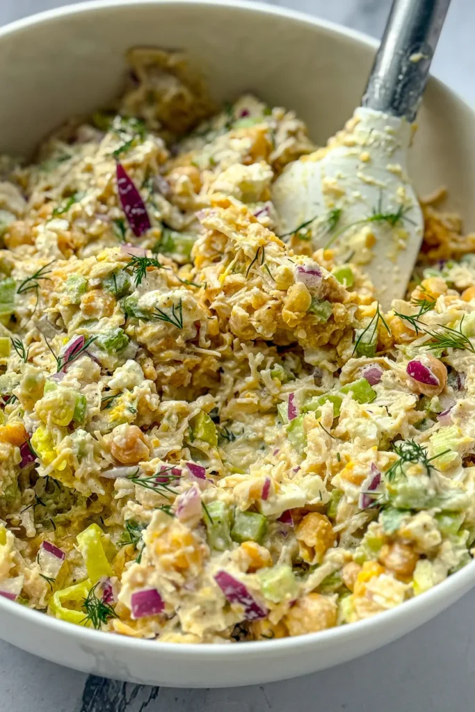 A birds-eye view of pepperoncini chicken salad in a large white bowl with a white spatula. 
