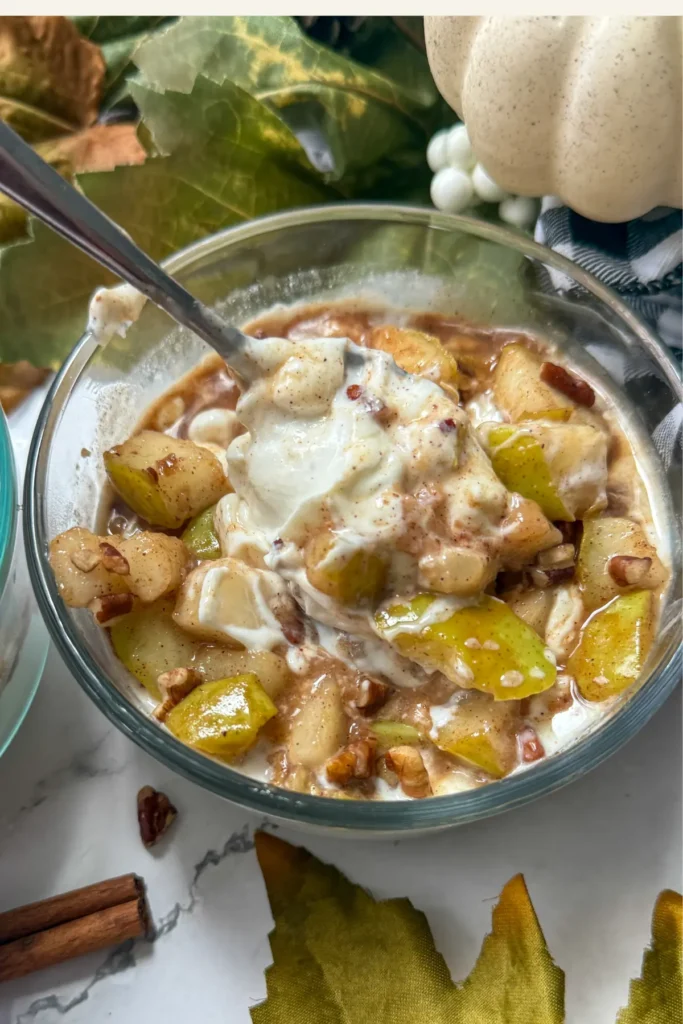 A yogurt bowl topped with spiced pears and walnuts on a fall-decorated table.