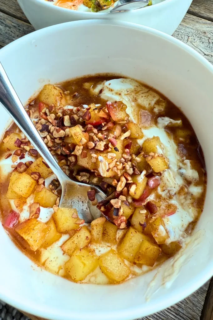 An apple pie yogurt bowl topped with cinnamon apples and pecans.