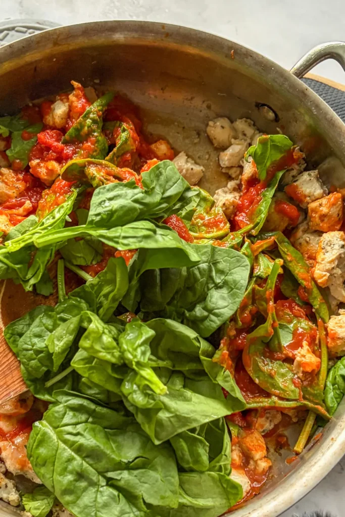 The marinara sauce, spinach and chicken cooking in a pan.
