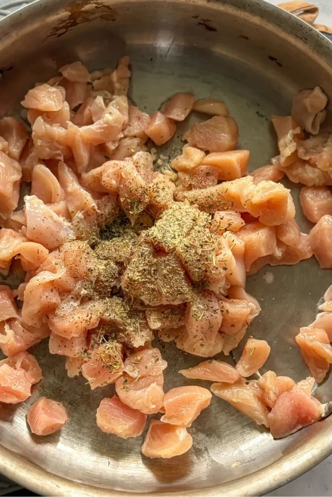 A pan with raw chicken cooking in it, with spices added.