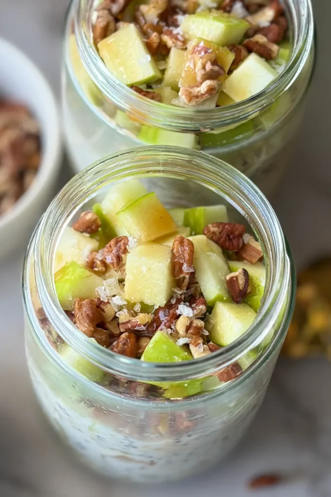 Two jars of overnight oats topped with diced apples, pecans, caramel and sea salt.