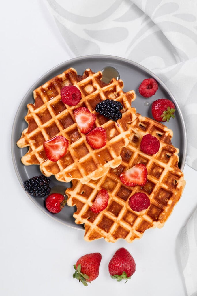 Two waffles on a plate topped with fruit on a counter.