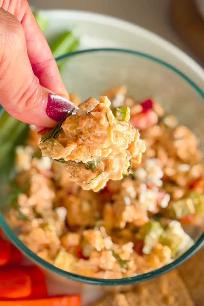 A close-up of a big scoop of the buffalo chicken dip with chickpeas on a Wheat Thin over a bowl of dip.