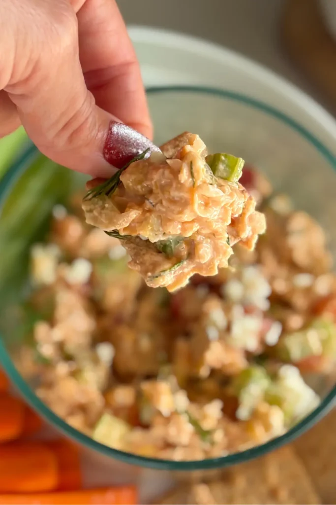 A Wheat Thin that has been dipped into the chicken dip over a snack plate.