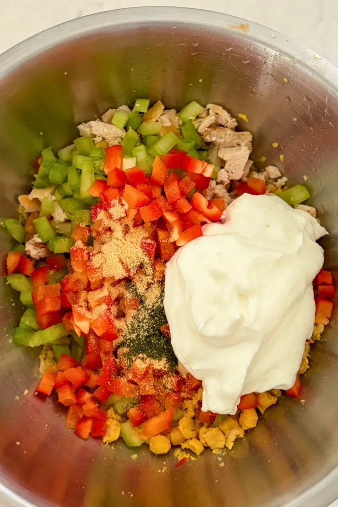 The chopped veggies, yogurt, chicken and spices in a mixing bowl.
