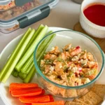 A loaded buffalo chicken dip snack plate with celery, carrots, and crackers on a table next to dip snack containers.