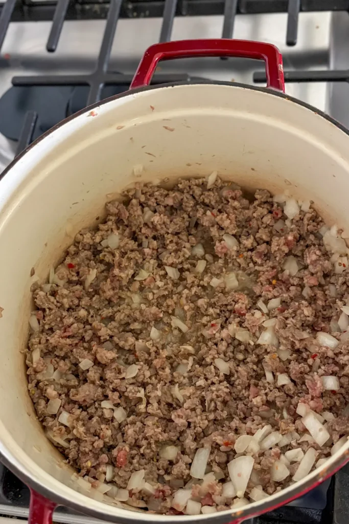 Browned Italian sausage with the diced onions, cooking in a Dutch oven.