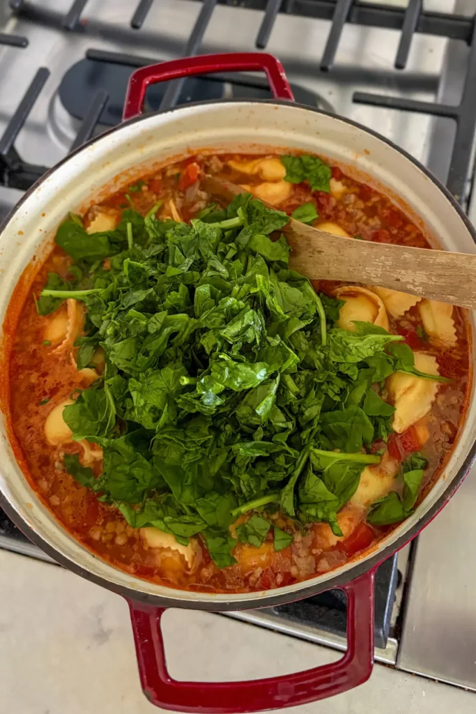 Adding in the spinach and tortellini to the soup after it has cooked.