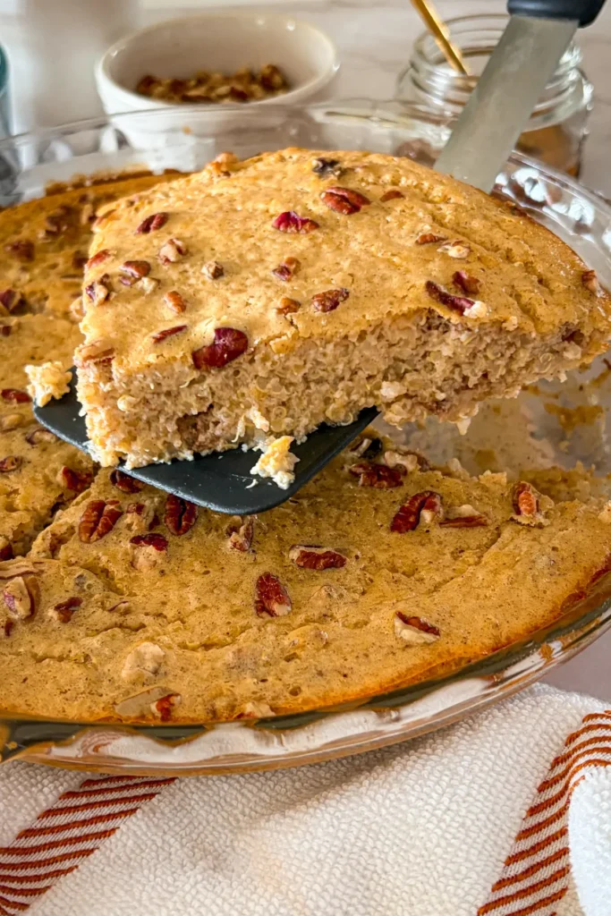 A slice of the quinoa breakfast bake on a spatula over a glass baking dish right out of the oven.