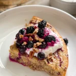 A slice of the maple pecan quinoa bake on a white plate, topped with Greek yogurt and mixed berries.