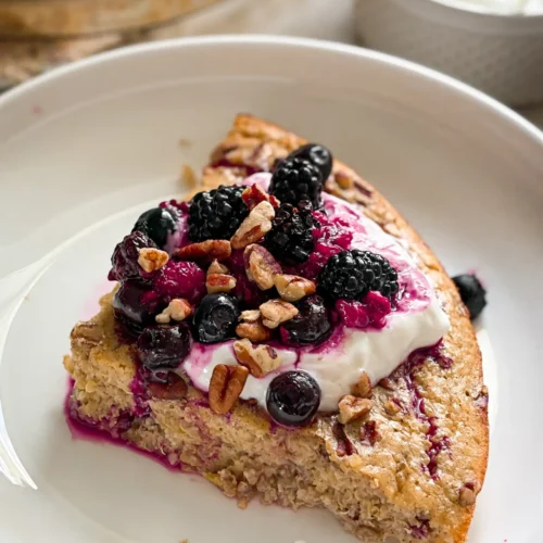 A slice of the maple pecan quinoa bake on a white plate, topped with Greek yogurt and mixed berries.