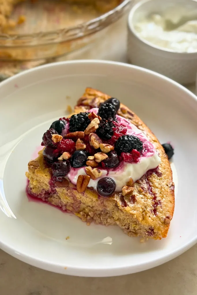 A slice of the maple pecan quinoa bake on a plate topped with yogurt and berries.
