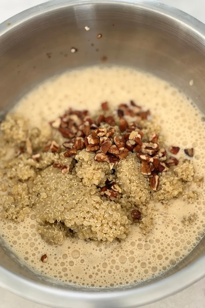 The quinoa and pecans addedd to the blended egg mixture in a bowl.